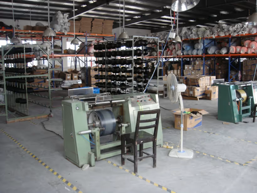 Textile machine with yarn creel and stocked webbing rolls in the factory materials area